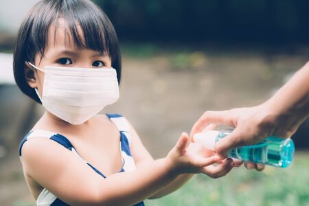 Mother take care son with face mask and sanitizer for protection disease flu or covid-19 outdoors, mom and child wearing medical mask clean hand for safety for outbreak of pandemic in public.の写真素材