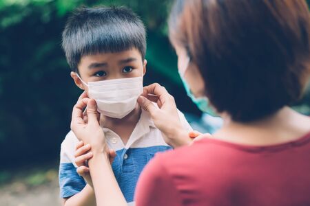 Mother take care son with face mask for protection disease flu or covid-19 outdoors, mom wearing on medical mask with child safety for protect outbreak of pandemic in public, medical concept.の写真素材