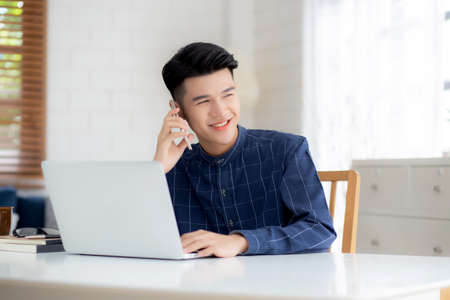 Young asian man talking phone and work from home with laptop computer, freelance using notebook to...