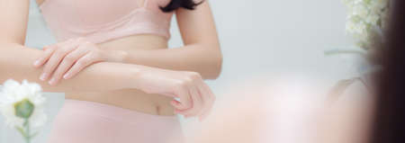 Beautiful sexy young asian woman looking mirror applying cream on arms and message, beauty girl applying body lotion skin care for soft, treatment and cosmetic with moisturizer, banner website.の写真素材
