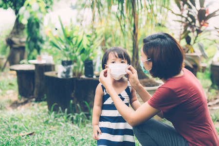 Mother take care daughter with face mask for protection disease flu or covid-19 outdoors, mom wearing on medical mask with child safety for protect outbreak of pandemic, medical concept.の写真素材