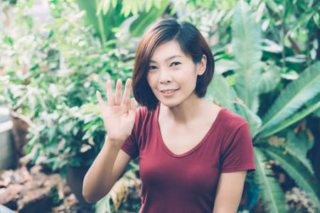Beautiful portrait young asian woman smiling waving hand in garden at home, Friendly girl and expression positive of emotion, hello and greeting, one person, happy female excited and cheerful.の写真素材