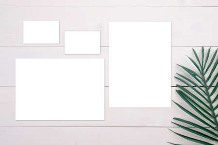 Blank paper sheet and name card mockup with copy space and leaf on wooden table, poster and...