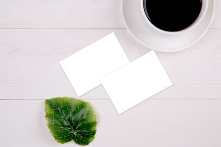 Business card mockup with copy space and leaf and cup of coffee on wooden table, name card blank and leaves decoration your design or branding, mock up template, nobody, flat lay, top view.の写真素材