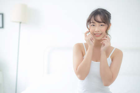 Portrait beautiful asian woman makeup of cosmetic, girl hand touch cheek and smile attractive, face beauty perfect with wellness in the bedroom at home with skin care and healthcare concept.の写真素材