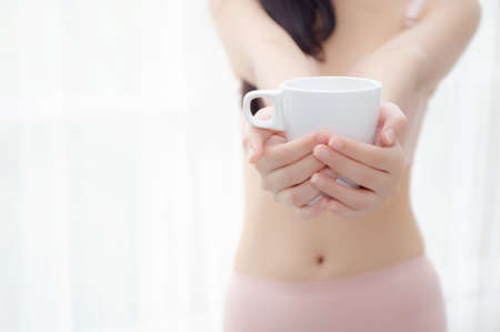 Closeup young asian sexy woman in underwear giving coffee near windows in the morning, girl with seductive figure fit serving beverage is breakfast for relax after wake up, lifestyle concept.の写真素材