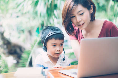 Young asian mother and son using laptop computer for study and learning together at home, boy...