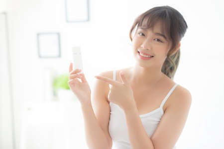 Beautiful portrait young asian woman holding and pointing presenting cream or lotion product, beauty asia girl show cosmetic makeup and moisturizing for skin care, healthy and wellness concept.の写真素材