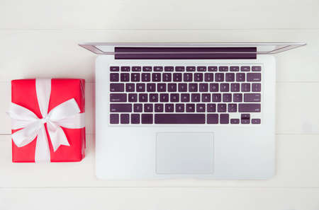 Red gift box and having laptop computer on wooden table, present giving for Christmas day or anniversary or birthday, season and celebrate, top view, flat lay, online shopping concept.の写真素材