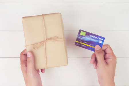 Hand of man holding credit card and online shopping for giving gift box with kraft paper on wooden...