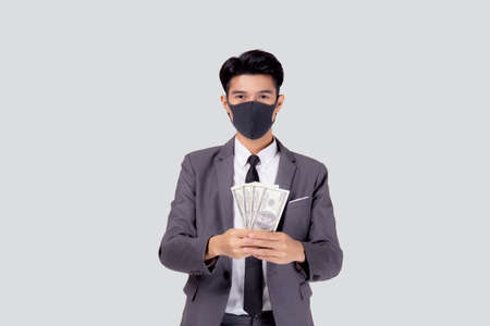Young asian businessman in face mask holding money dollar isolated on white background, pandemic and...