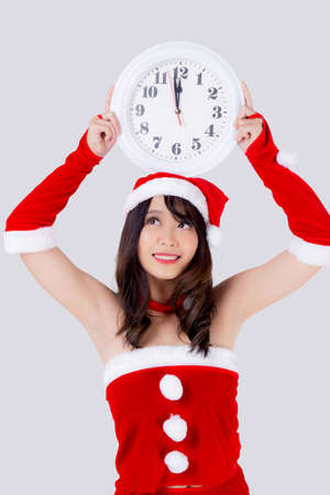 Beautiful portrait young asian woman in Santa dress holding clock with excited in xmas holiday isolated on white background, beauty asia girl celebrating success in festive Christmas day or new year.の写真素材