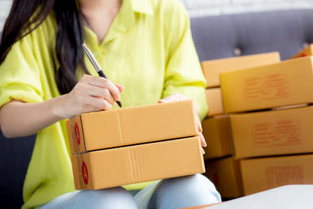 Closeup hand of young asian woman writing address on parcel box at home for delivery order to...