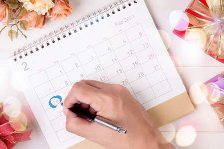 Hand writing with marker on calendar reminder with memo 14 February Valentine day on desk with blur bokeh background, appointment for plan surprise of love and romance, top view, holiday concept.の写真素材