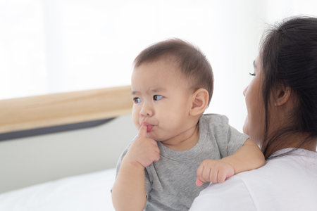 Young asian mother holding little baby girl together in the bedroom at home, mom carry child and...