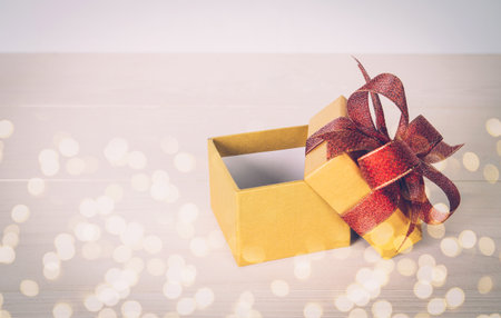 Gold gift box open on wooden table with bokeh background, love and romance, presents in celebration...