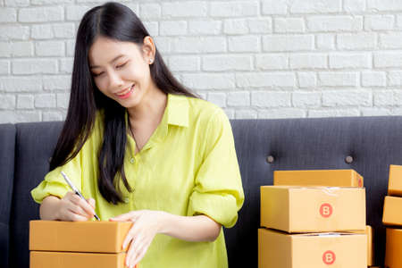 Young asian woman writing address on parcel box at home for delivery order to customer, shipping and logistic, merchant online and seller, business owner or SME, online shopping and e-commerce.の写真素材