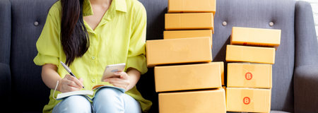 Young asian woman is entrepreneur looking phone and writing order of customer with online on...
