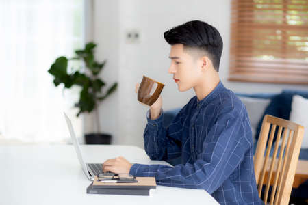 Young business man working from home with laptop computer on desk, freelance male sitting stay home using notebook for communication and relax on table, entrepreneur in startup business, new normal.の写真素材
