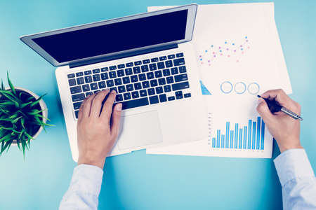 Hand of businessman looking documents report statistic financial with graph and chart and laptop computer on deskの写真素材