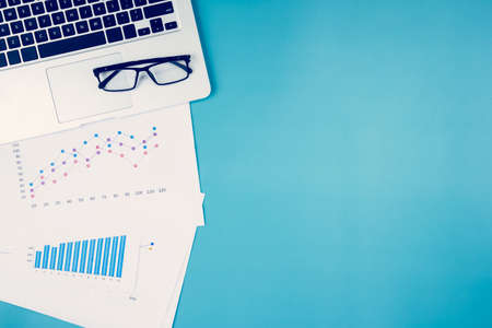 Laptop computer and documents report statistic financial with graph and chart and glasses on deskの写真素材