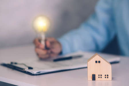 Real estate agent holding bulb and contract agreement of real property document on desk, house broker and planning investment, businessman thinking idea with lightbulb and paperwork, business concept.の写真素材