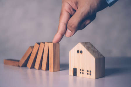 Hands of businessman stop risk about home with block wooden and safety, investment and insurance about real estate and property, planning and strategy, loan and debt of house, business concept.の写真素材