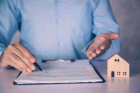 Real estate agent holding home and signing contract about agreement of real property on desk, house broker and planning investment, businessman writing on document form rent house, business concept.の写真素材