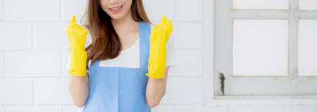 Portrait young asian woman is housekeeper in rubber gloves and apron for protection at home, uniform of maid, cleaning and washing, girl standing worker positive, one people, lifestyle concept.の写真素材