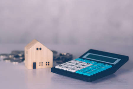 Investment about home with calculator and model house and coins on desk, property and real estate and mortgage, loan and finance, financial saving and account for residential, business concept.の写真素材