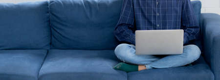 Young asian businessman smile and work from home with laptop computer online to internet on sofa in living room, freelance man using notebook on couch with comfort, new normal, lifestyle concept.の写真素材