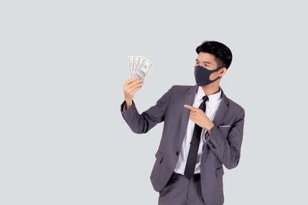 Young asian businessman in  face mask holding money dollar isolated on white background, pandemic and crisis of economic, business man in medical mask and investment during disease covid-19.の写真素材