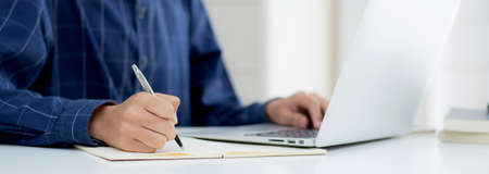 Closeup hand of business man writing on note while using laptop computer on desk at home, male...