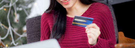 Young asian woman online shopping in Christmas with credit card on laptop computer, female buying...