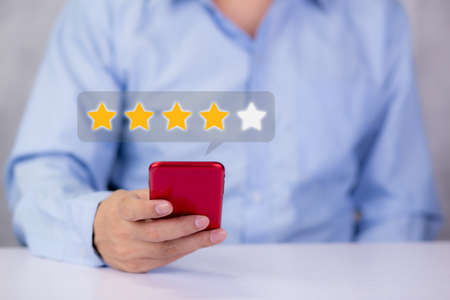 Customer holding phone and pressing star icon for vote score review and feedback with quality and...