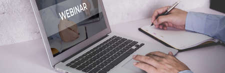 Hand of man watching webinar on laptop computer and writing on notebook for learning, education with...