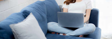Young asian business woman in face mask work from home on laptop computer online to internet in living room, girl in quarantine for pandemic, stay home, new normal.の写真素材