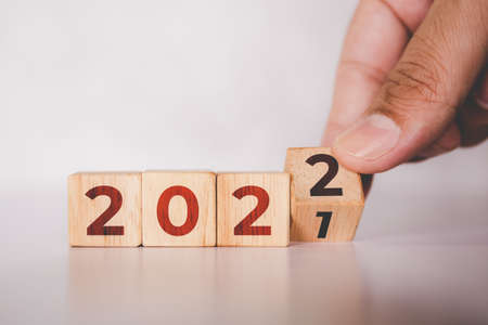 Hands flipping cube wooden block with text year 2022, beginning and trend, calendar and time, determination target and planning for achievement, motivation and aspirations, business concepts.の写真素材