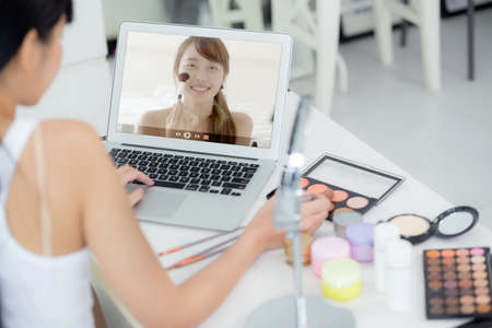 Beauty of young asian woman with learning makeup with brush on cheek on laptop computer with tutorial course online, female teaching and explain make up with cosmetic on streaming social media.の写真素材