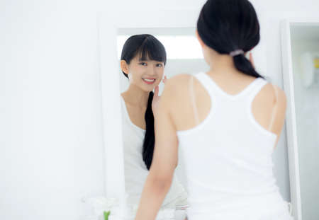 Beautiful face of young asian woman with happy smiling and touch cheek looking mirror with charming, makeup of beauty facial girl with skincare and cosmetic treatment, skin care and healthy concept.の写真素材