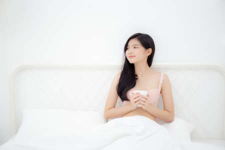 Beautiful young asian sexy woman in underwear drinking coffee in the morning on bed at bedroom, asia girl with seductive figure fit drinking beverage for relax after wake up, lifestyle concept.の写真素材