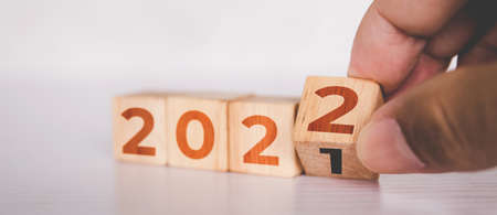 Hands flipping cube wooden block with text year 2022, beginning and trend, calendar and time, determination target and planning for achievement, motivation and aspirations, business concepts.の写真素材