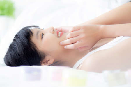 Beautiful of young asian woman smiling and lying on bed at bedroom, beauty of girl touch cheek with hygiene and healthy, cream and lotion, cosmetic and makeup, skin care and lifestyles concepts.の写真素材