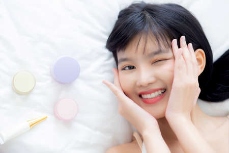 Beautiful of young asian woman smiling and lying on bed with cosmetic at bedroom, beauty of girl with hygiene and healthy, cream and lotion and skin care, top view, skincare and lifestyles concepts.の写真素材