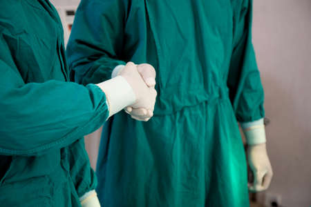 Teamwork of doctor and assistant handshake with success together at hospital, agreement and partner of surgeon, team of surgical shaking hands with confident at operation room, medical and health.の写真素材