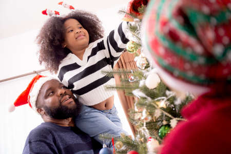 Happy family with father carry daughter decorating ornament on Christmas tree together at home,...