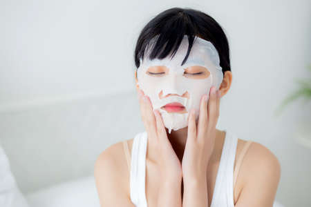 Beautiful young asian woman with sheet facial mask at home, beauty girl applying cosmetic and makeup with skin care face for wrinkle, skincare treatment and moisturizer, health and wellness.の写真素材