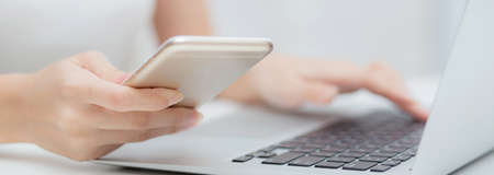 Closeup hand of young woman working laptop computer and reading smartphone on internet online on...