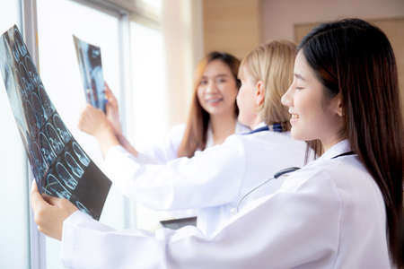 Group of team doctors examining x-ray film about skull and skeleton of patient for checking disease while discussion at hospital, doctors and assistant talking and conference, medical concept.の写真素材