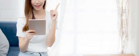 Young attractive asian woman resting using browsing tablet computer on sofa at home, happy girl...